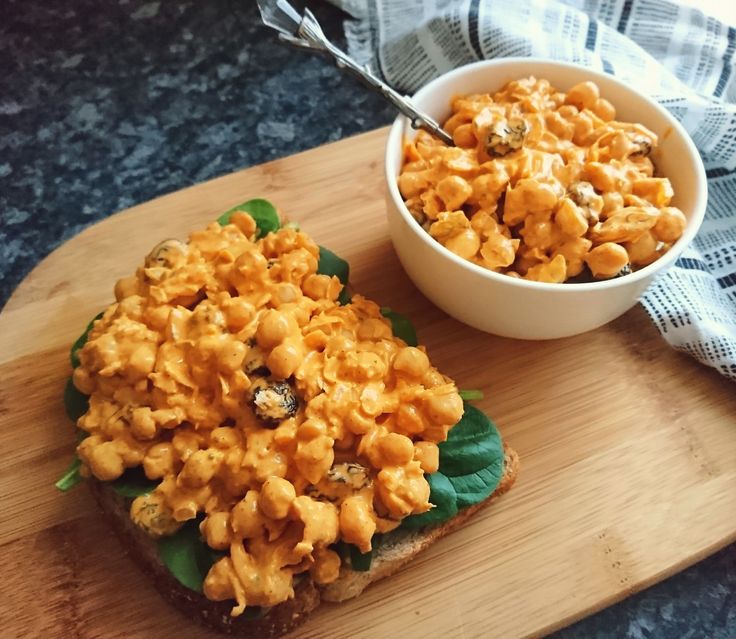 a wooden cutting board topped with a sandwich and bowl of macaroni salad