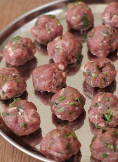 some meatballs are sitting on a metal plate with green garnish and sprinkles