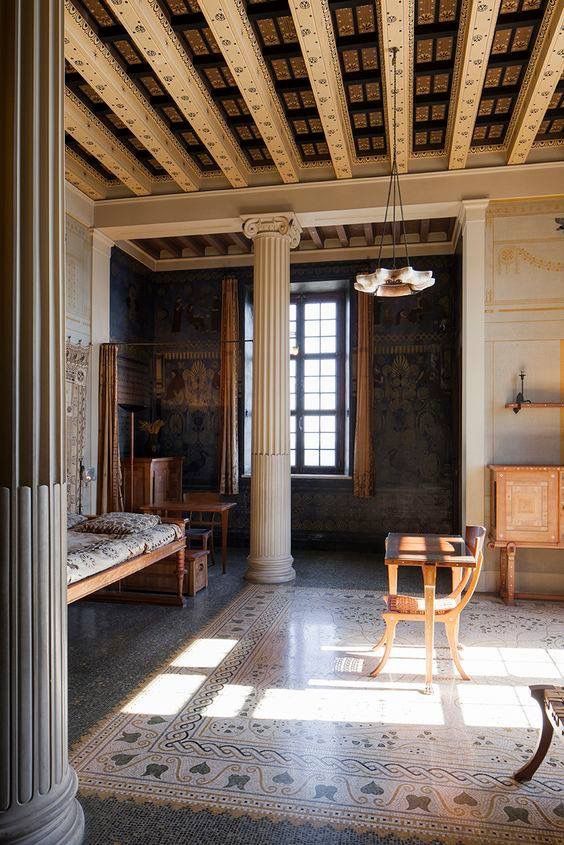 an old room with columns and paintings on the walls, floor to ceiling windows, and a bed