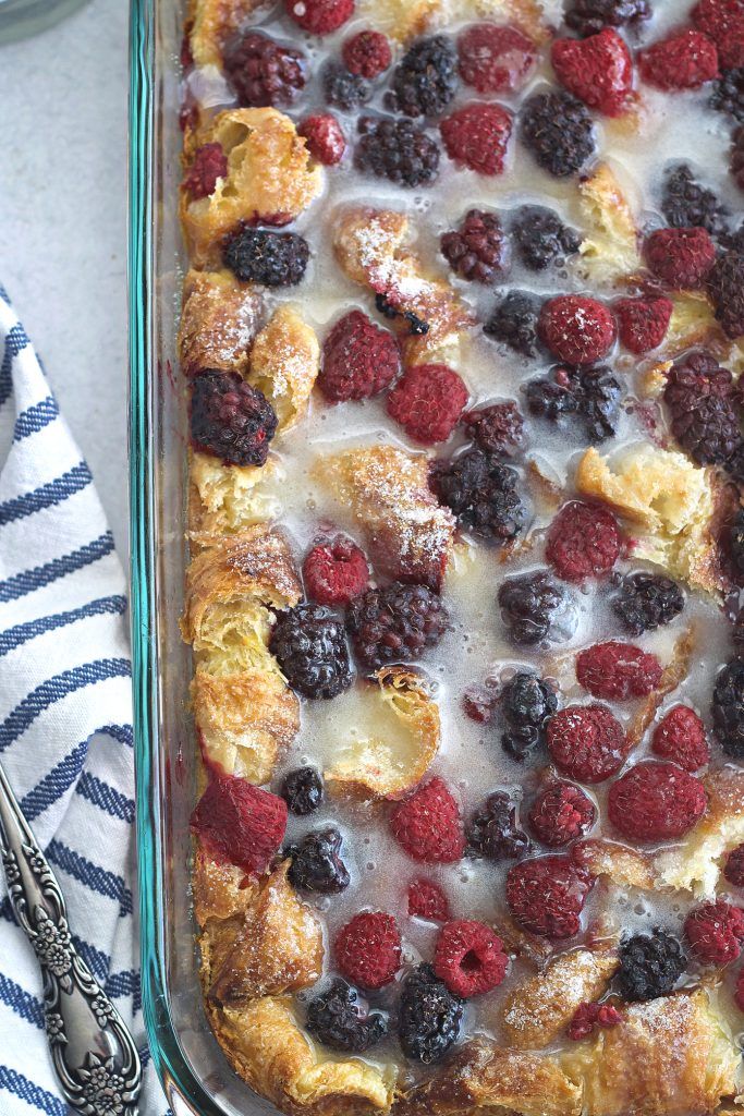 a casserole with berries and cream in a glass dish next to a spoon