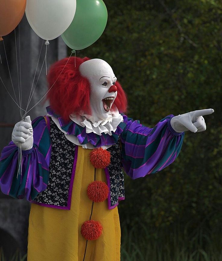 a clown holding balloons and pointing at something