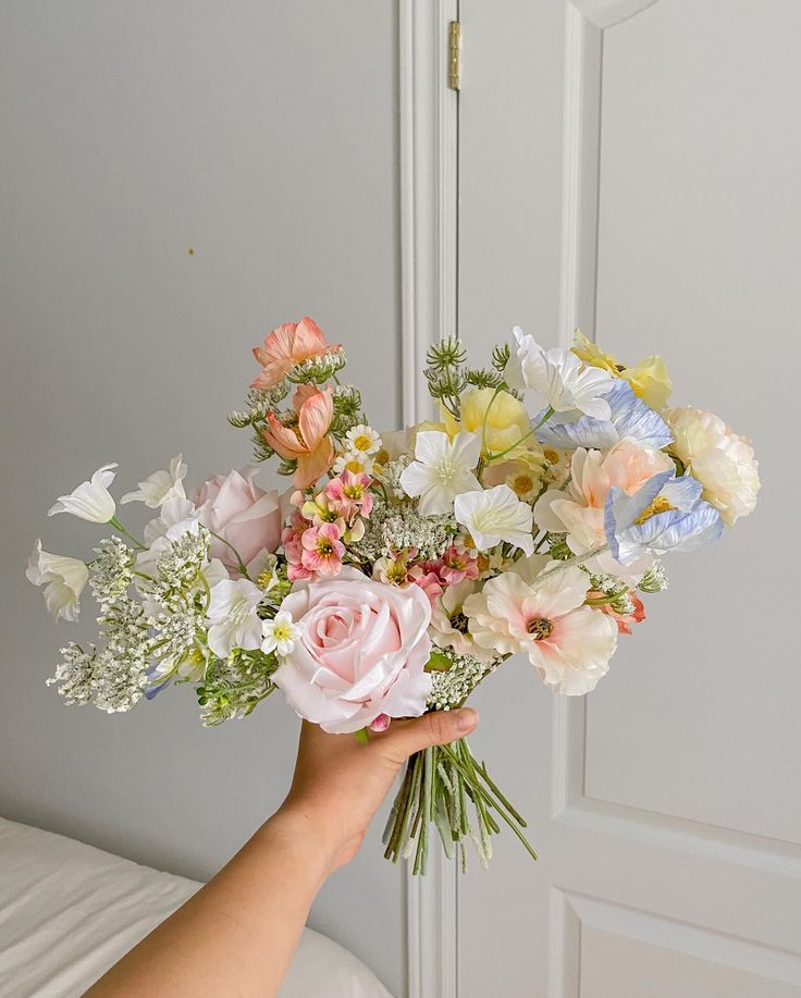 a hand holding a bouquet of flowers in front of a white door with blue and pink accents