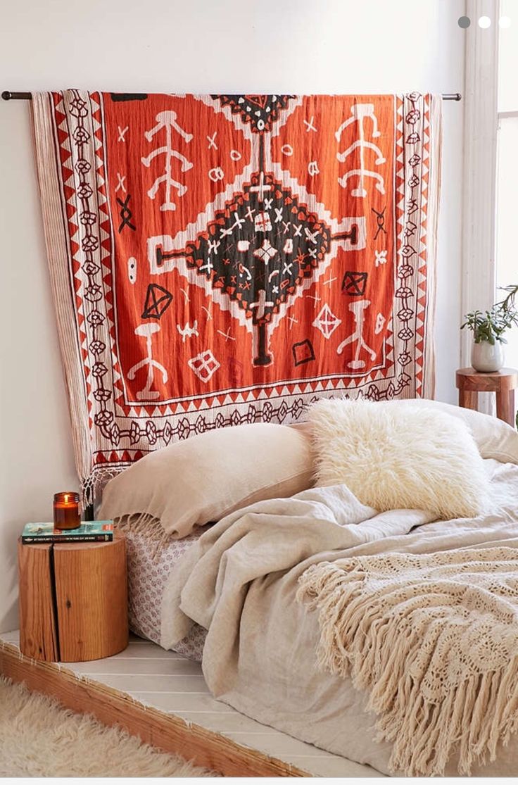 a bed with an orange and white tapestry hanging over it's headboard next to a window