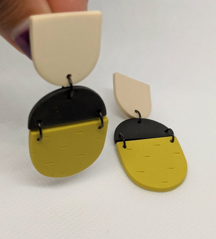 a pair of yellow and black earrings being held by a person's hand on a white surface