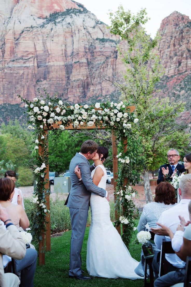 a bride and groom kissing in front of a mountain backdrop at their outdoor wedding ceremony