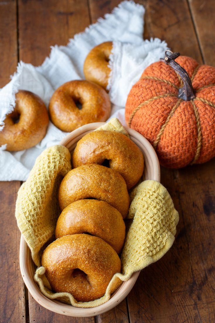 a bowl filled with doughnuts next to a small pumpkin on a wooden table