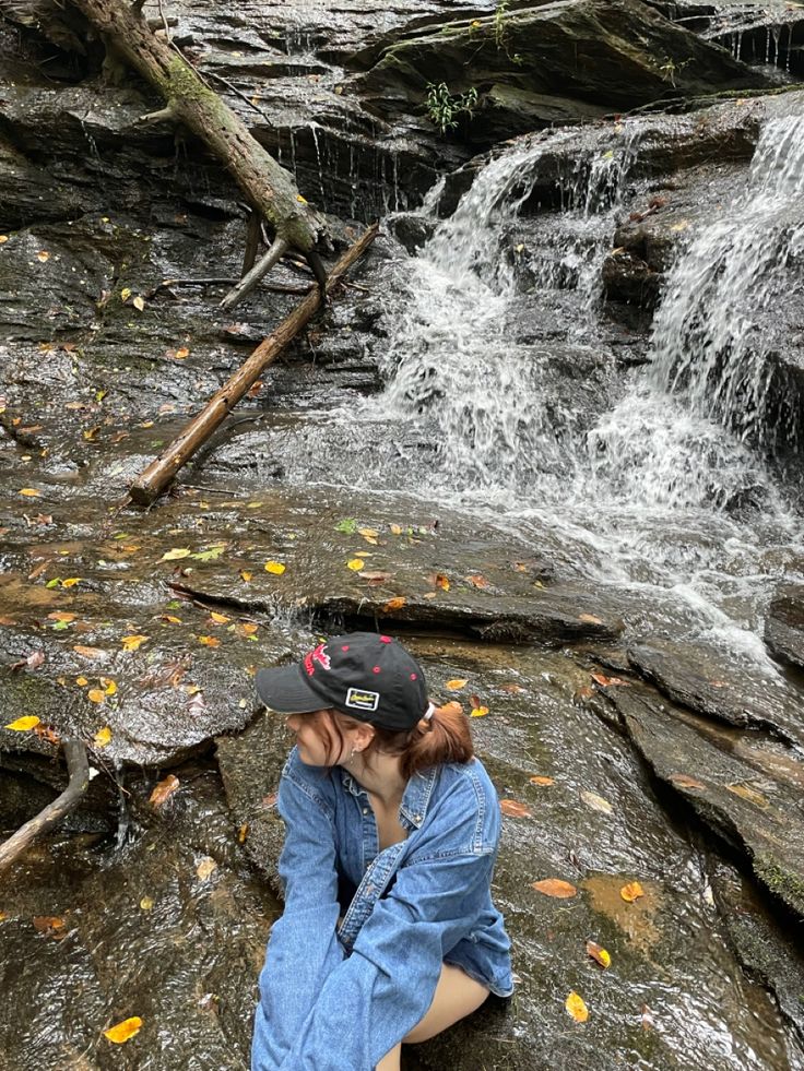 a woman sitting on top of a rock next to a waterfall