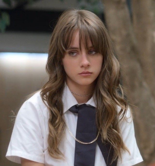 a woman with long hair wearing a tie and white shirt sitting in front of a tree