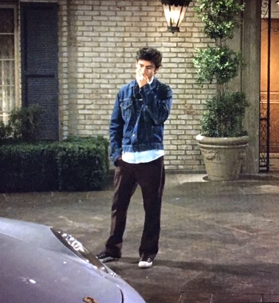 a man talking on a cell phone while standing next to a car in front of a building