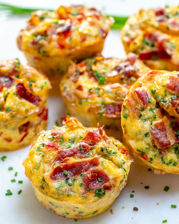 several breakfast muffins with bacon and chives on a white plate next to an egg