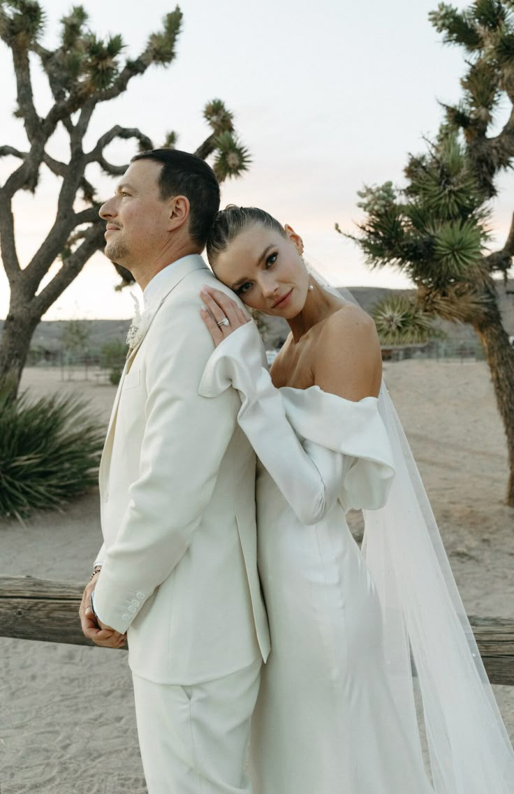 a man and woman standing next to each other in front of some trees on the beach