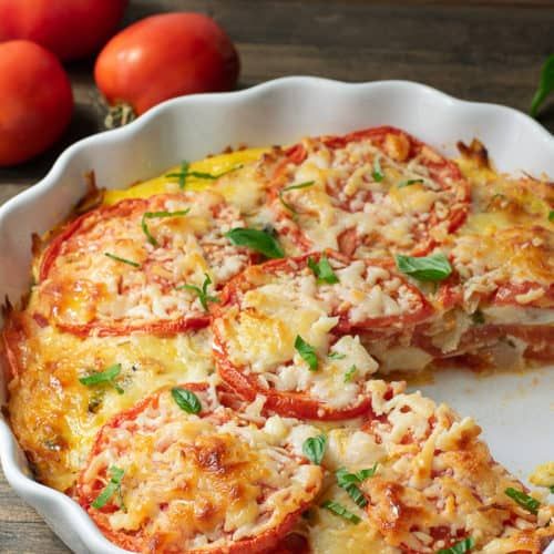 a casserole dish with tomatoes and cheese in it on a wooden table next to other food items