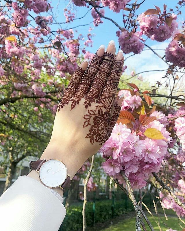 a woman's hand with henna on it in front of pink flowers and trees