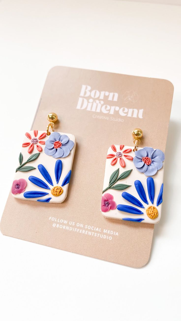 a pair of earrings with flowers painted on the front and back of them, sitting on top of a card