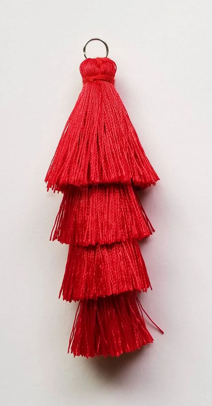 a red tasseled keychain hanging on a white wall in the shape of a christmas tree