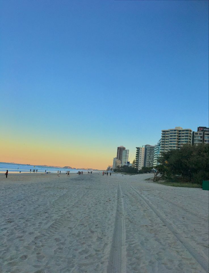 people walking on the beach at sunset with tall buildings in the backgroung