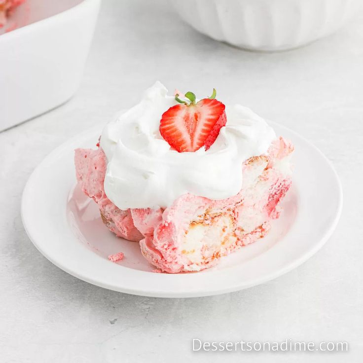 a piece of strawberry shortcake on a plate with whipped cream and strawberries in the background