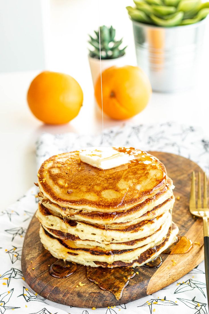 a stack of pancakes sitting on top of a wooden cutting board next to oranges