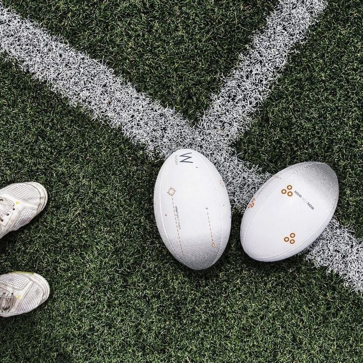 two white footballs sitting on top of a field next to a pair of shoes