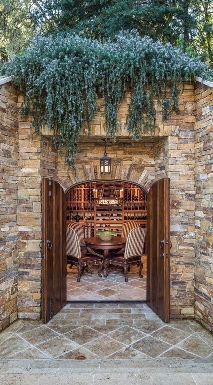 an outdoor dining area with stone walls and doors leading to a wine cellar in the background