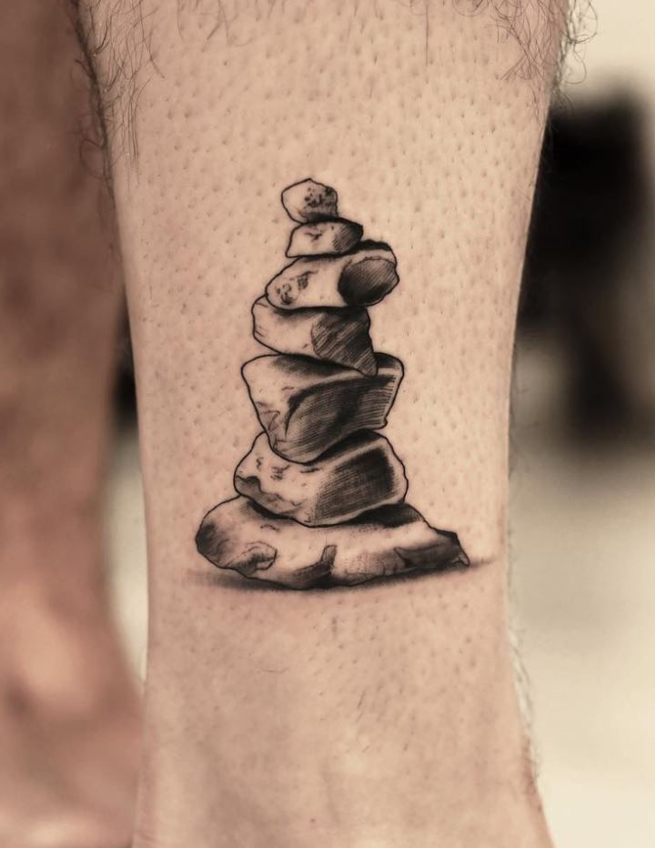 a man's foot with a stack of rocks tattoo on the side of his leg