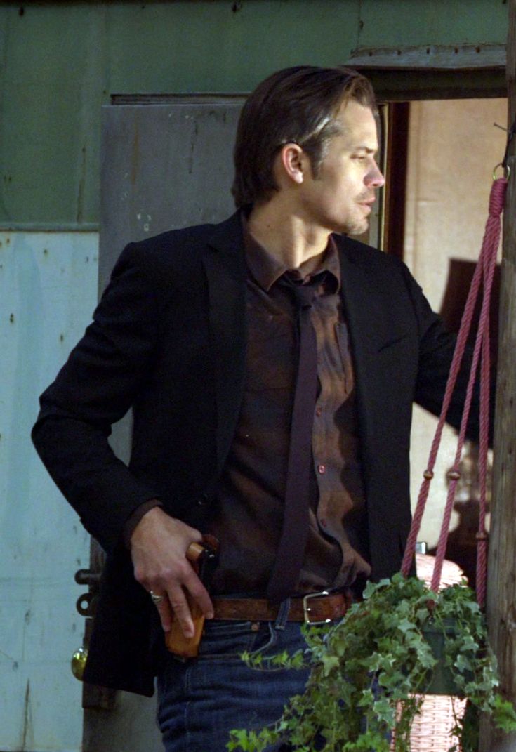 a man wearing a suit and tie standing next to a plant in a hanging pot