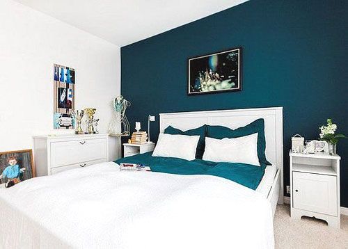 a bedroom with blue walls and white bedding in the center is decorated with pictures on the wall