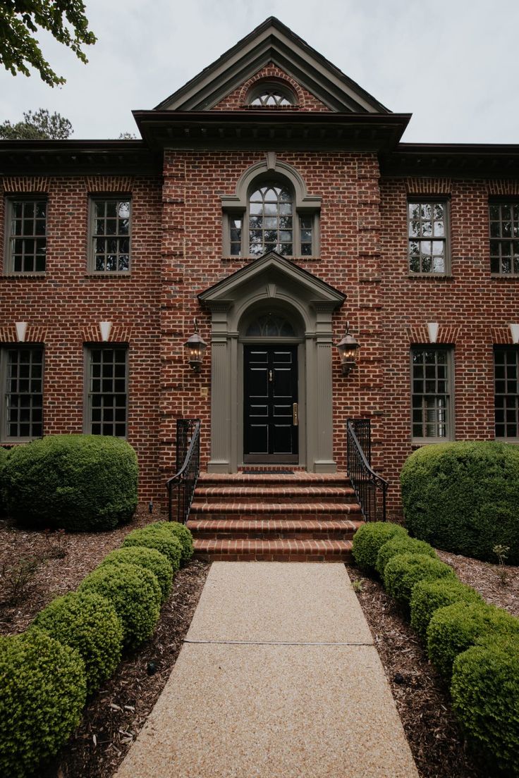 an old brick house with steps leading to the front door and two large bushes on either side