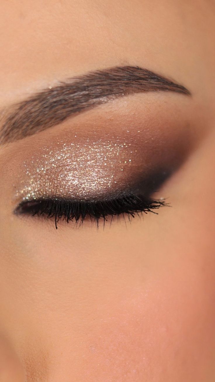 a woman's eye with gold glitter on her eyeshade and lashes, close up