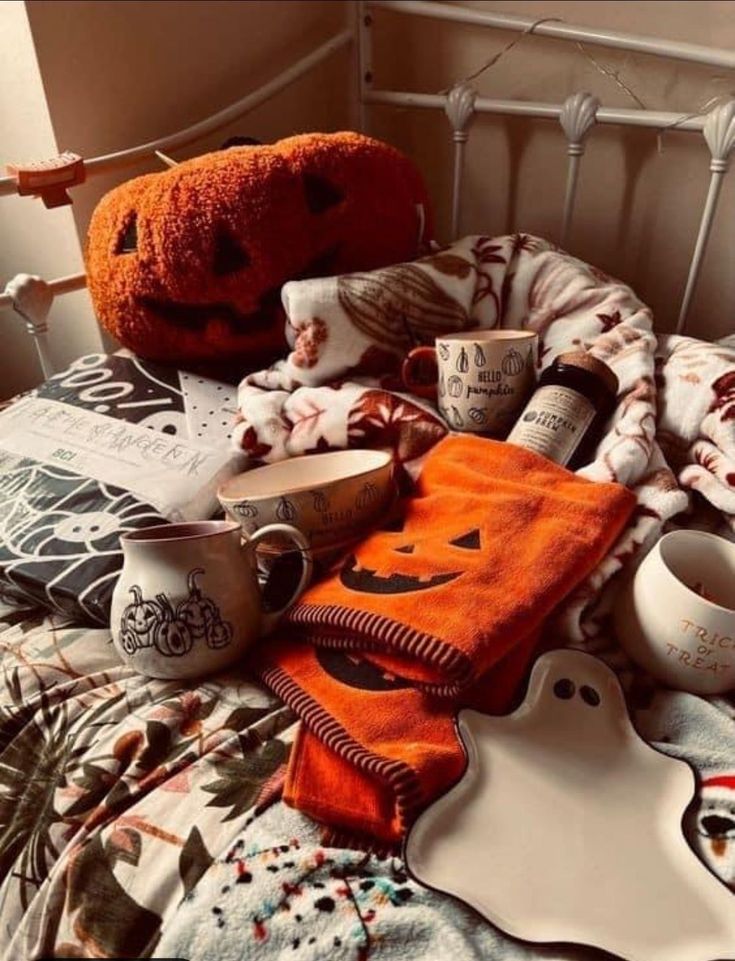 a bed topped with lots of halloween items and cups next to a pumpkin shaped pillow