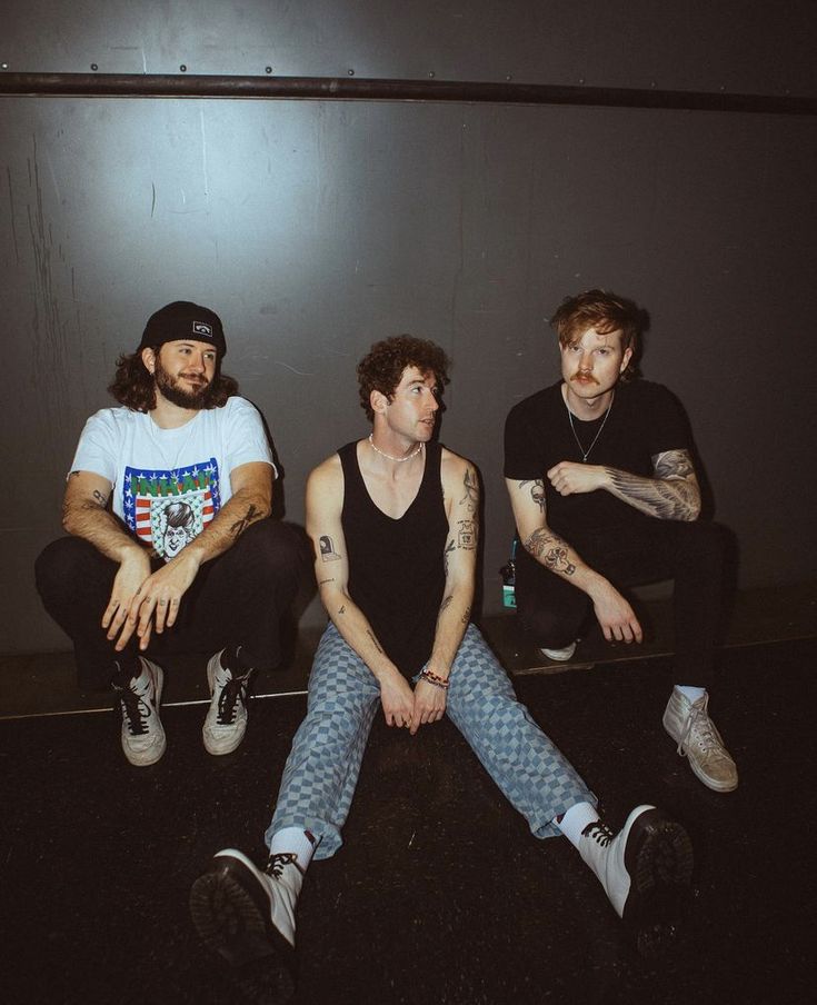 three young men sitting on the floor in front of a wall with their arms crossed