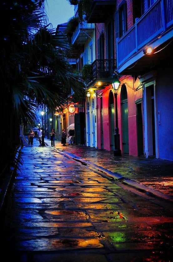 an empty city street at night with people walking on the sidewalk and colorful buildings in the background