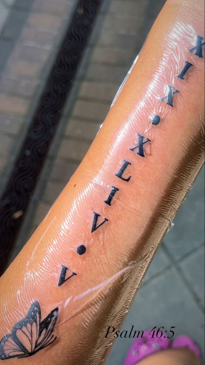 a woman's arm with roman numerals and butterfly tattoos on her forearm