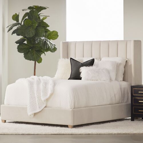 a bed with white sheets and pillows in a room next to a plant on the floor