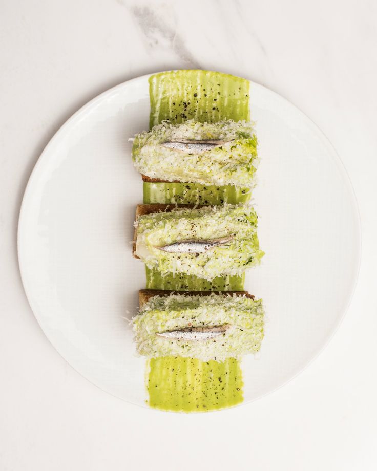 a white plate topped with cucumber slices covered in green sauce and sprinkles