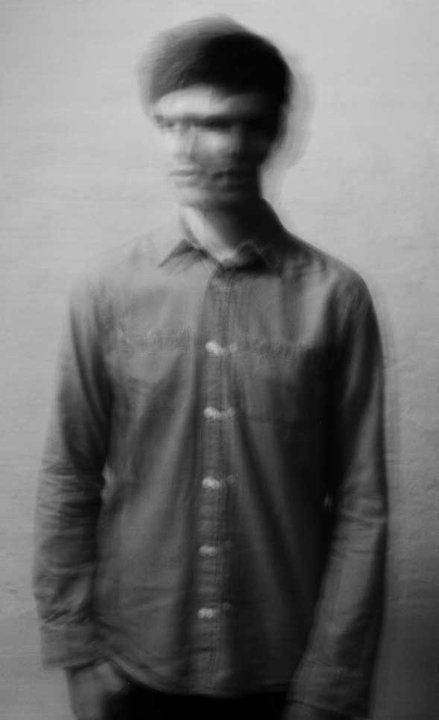 a man standing in front of a wall with his face obscured by the shirt on