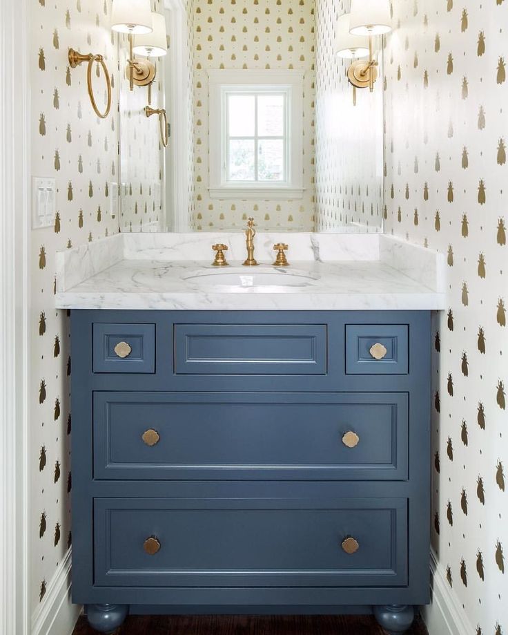 a bathroom vanity with blue drawers and white counter top, gold accents on the wall