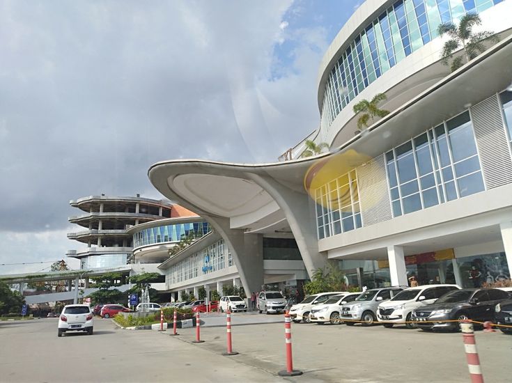 cars are parked in front of a large building with curved roof and glass windows on the top floor