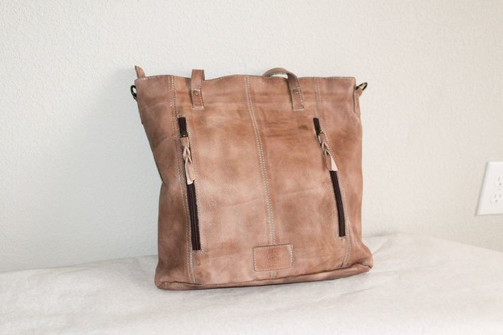 This rustic, leather travel tote is ideal for organizing your belongings on the go. Its brass brads, double exterior pocket, exterior conceal and carry pocket, interior double pocket, interior zipper pocket, and lined interior provide generous space for all your essentials. The perfect blend of functionality and style. About 11” x 14” Shipping on custom items takes 8-10 business days. Rugged Leather Bag With Zipper Pocket, Rugged Brown Bag With Zipper Pocket, Rugged Rectangular Shoulder Bag For Everyday, Distressed Brown Tote Shoulder Bag For Travel, Everyday Rugged Rectangular Shoulder Bag, Brown Leather Weekender Bag With Zipper Pocket, Travel Shoulder Bag With Leather Backing In Distressed Brown, Everyday Rugged Soft Leather Bag, Rugged Everyday Soft Leather Bag