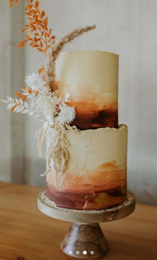 a three tiered cake with orange and white frosting on a wooden table in front of a wall