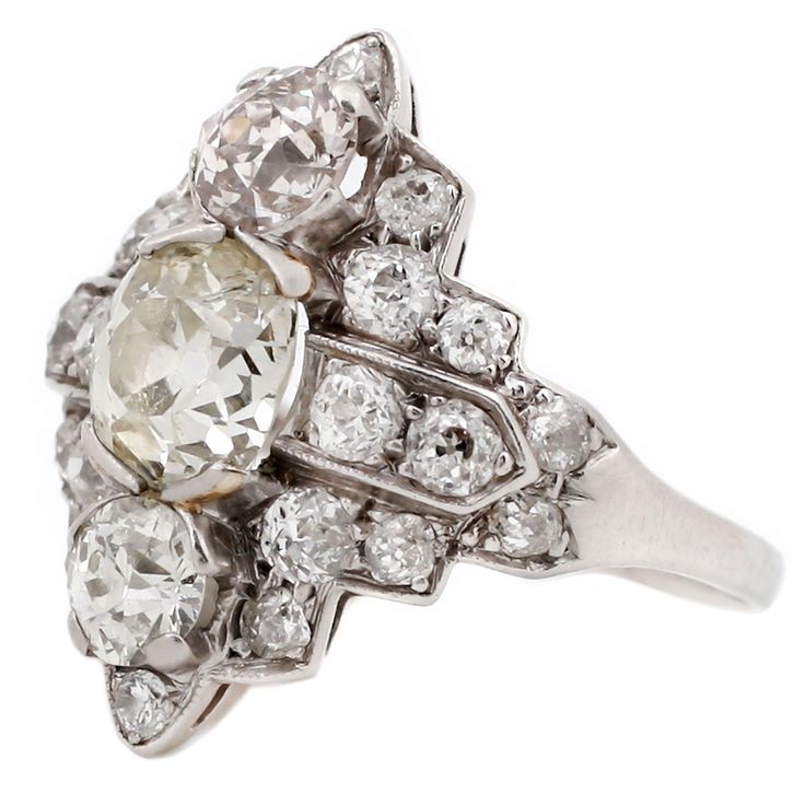 This show stopping antique ring hails from the 1920s and exudes all the art deco elegance of the era. Rendered in pure platinum, brilliant white diamonds make an architectural design around a 1.65ct old-mine-cut stone. Designed to make a statement then and now, this bold ring is one-of-a-kind. Appraisal available upon request. Stones: Center: 1.65ct White Old Mine Cut Diamond (Color O-P, SI-1), Top/Bottom stones: Two White Brilliant Cut Diamonds (Total .81tcw, Color I-J, Clarity VS1-SI1), Sides: Art Deco Diamond Ring With Prong Setting, Art Deco Platinum Diamond Ring With Brilliant Cut, Antique White Diamond Ring In Platinum, Art Deco Platinum Ring With Rose Cut Diamonds, Art Deco Platinum Rings With Rose Cut Diamonds, Art Deco Platinum Diamond Ring In Diamond White, White Platinum Diamond Ring In Art Deco Style, Antique White Diamond Platinum Ring, Art Deco Platinum Diamond Ring With Single Cut Diamonds