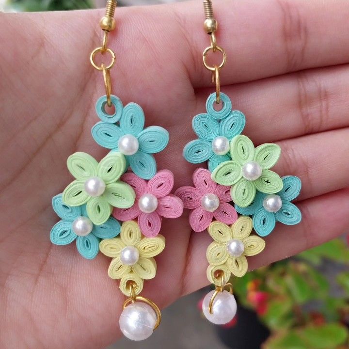 a pair of earrings with flowers and pearls on them are being held in someone's hand