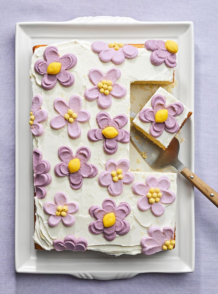 a white plate topped with a cake covered in purple and yellow flowers next to a knife