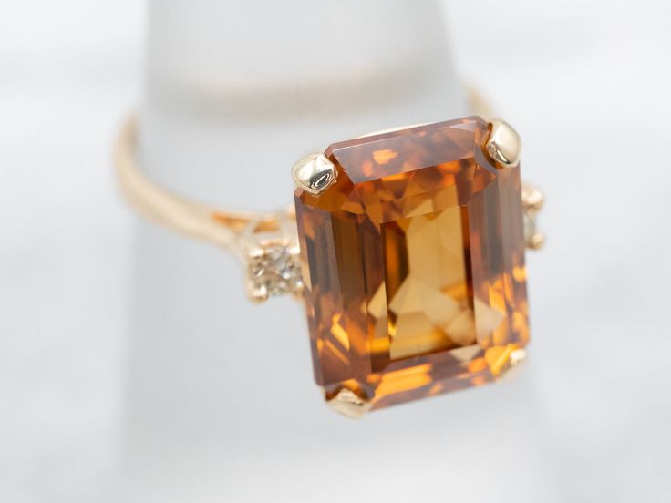 This mounting dates to the Retro era, although we've replaced the center gemstone. The design is lovely, and simple but graceful. We've set this vintage mounting with a sparkling, beautiful golden zircon! This stone is from Sri Lanka, the source of some of the most richly colored, brilliant zircons in the world. Natural zircon was a common sight in the jewelry stores of the 1930s, in fact, it's one of the original birthstones for December, but nowadays it's been overshadowed by cubic zirconia. Similar name, but the two stones are not related in any way.Metal: 14K Yellow GoldGem: Orange ZirconGem Measurements: 12.6 x 10.1 mm, Emerald CutAccents: 2 Diamonds totaling .09 Carats, VS in Clarity, I in ColorRing Size: 6.50Marks: “14K” Stamped on the inside band Classic Topaz Ring With Diamond And Gemstone Accents, Classic Topaz Diamond Ring With Accent Stones, Classic Diamond Ring With Accent Stones, Classic Topaz Gemstones With Accent Stones, Classic Citrine Birthstone Ring With Center Stone, Classic Topaz Ring With Gemstone Accents, Classic Topaz Birthstone Ring With Center Stone, Cut Orange, Retro Era