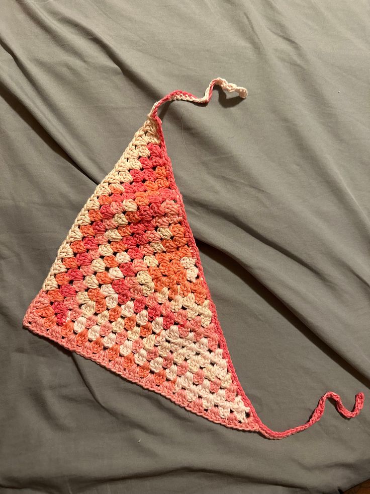 a crocheted triangle laying on top of a gray bed sheet with pink and white flowers