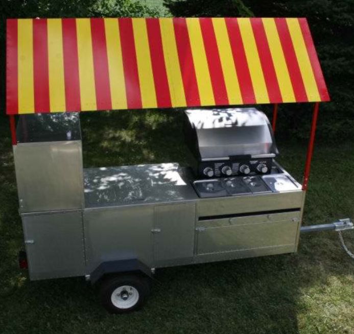 an outdoor grill with a red and yellow striped awning over it's top