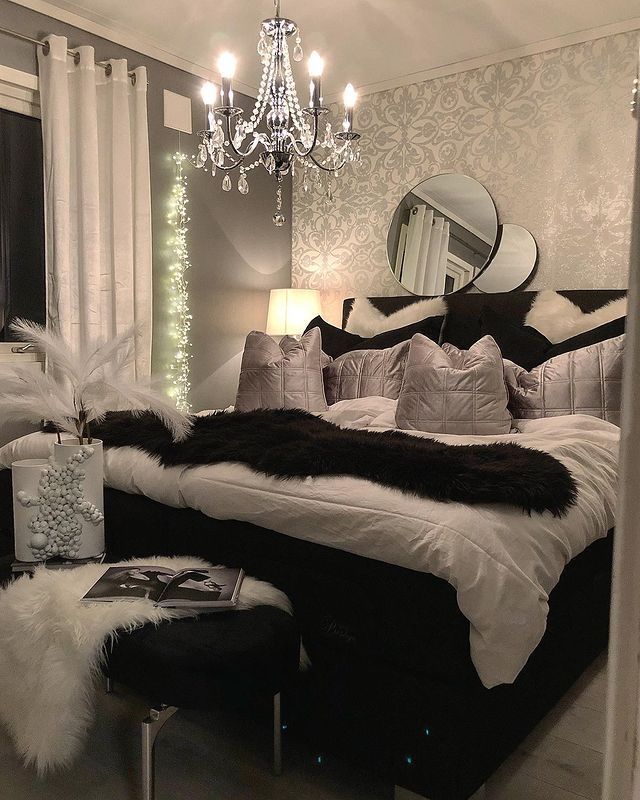 a black and white bedroom with a chandelier hanging from the ceiling, pillows on the bed