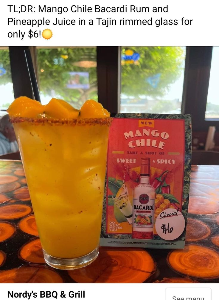 a tall glass filled with orange juice sitting on top of a table next to a book