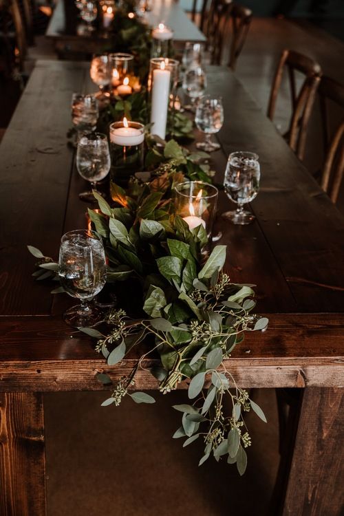 a long wooden table with candles and greenery on the top, surrounded by wine glasses