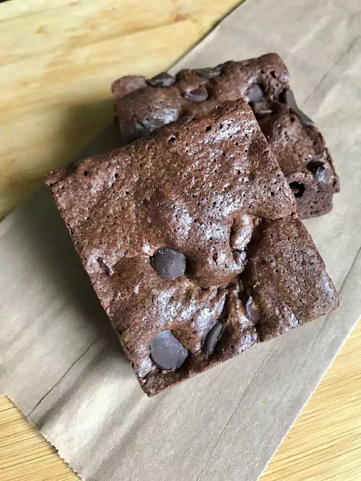 two brownies sitting on top of a piece of wax paper next to a wooden table